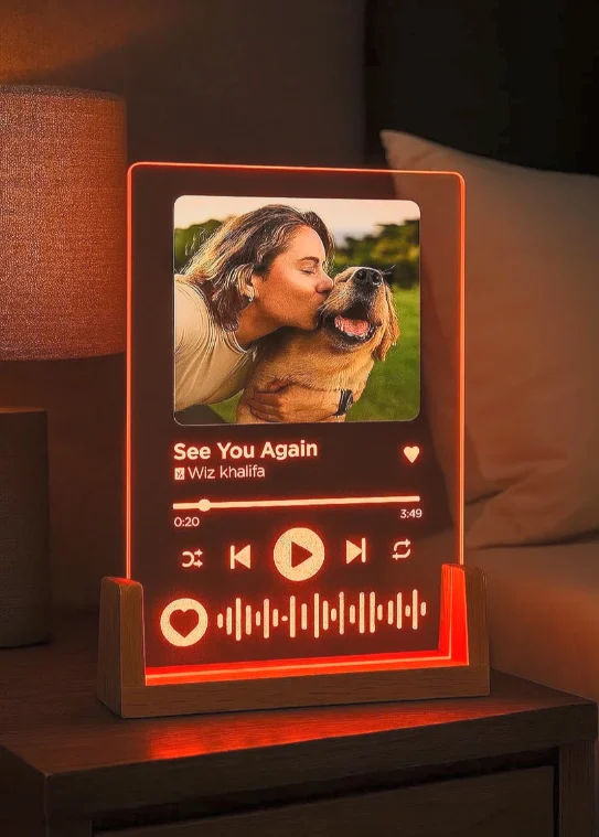 Personalised acrylic LED music plaque with a photo of a woman kissing a dog, glowing orange on a bedside table