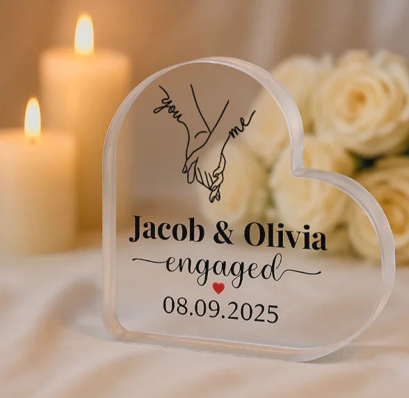 Plaque en acrylique personnalisée en forme de cœur imprimée « Jacob & Olivia engaged » et une date, avec, en arrière-plan, des bougies et des roses