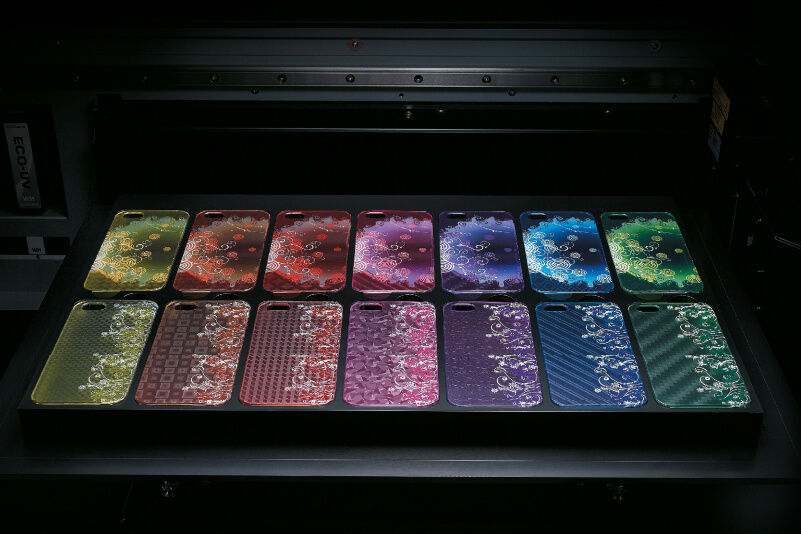 Una impresora de mesa plana con fundas de móvil multicolores personalizadas