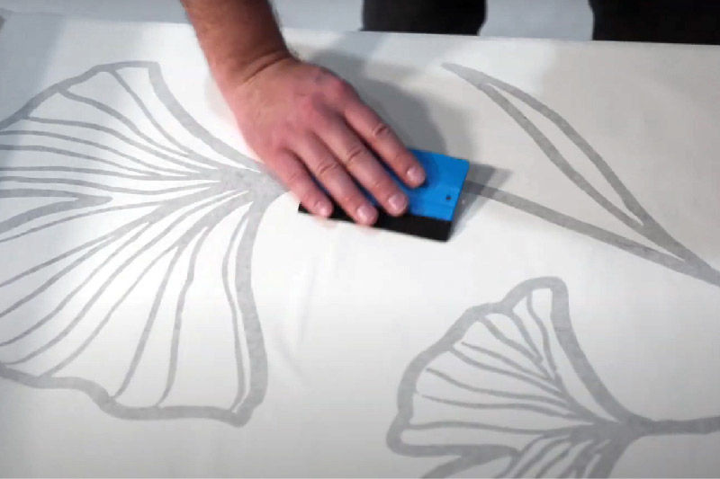 Using a squeegee to apply the application tape to the vinyl