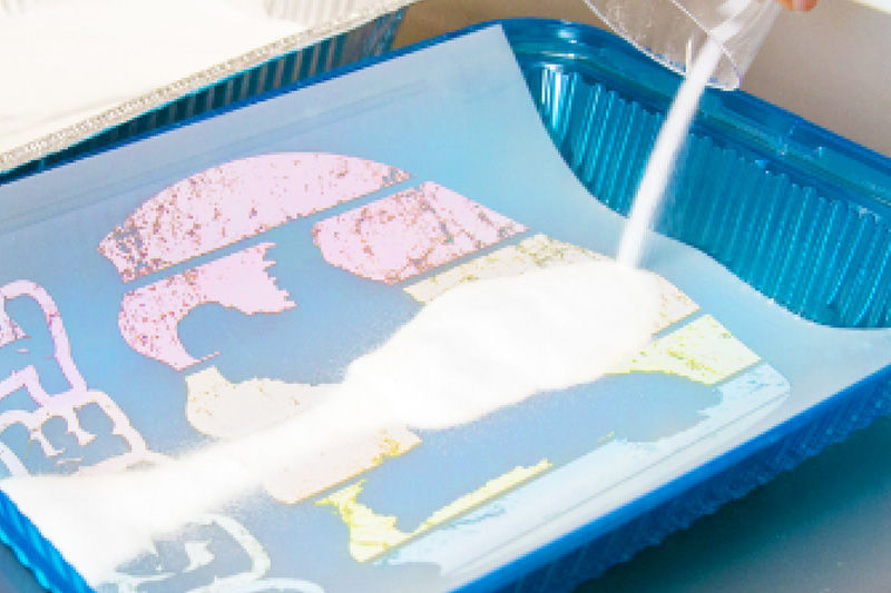 Apply the adhesive powder, making sure the ink is covered and the excess is removed